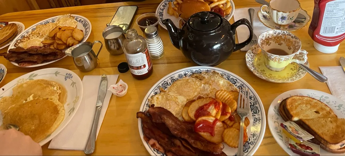 A table of breakfasts: pancakes, bacon, eggs, toast and a brown teapot