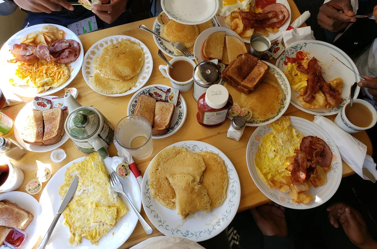 Plates of pancakes, eggs and bacon shared across a table